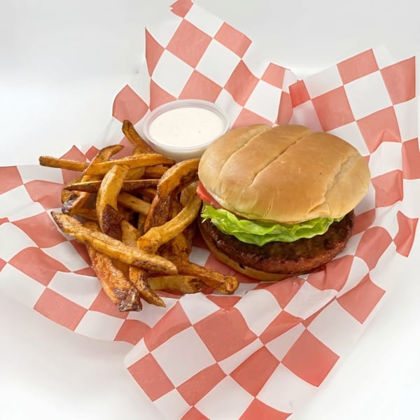 A hamburger with lettuce and tomato, fries, and a dipping sauce in a red and white checkered basket.