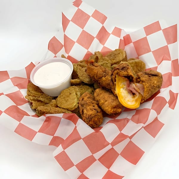 Fried pickles and cheese-filled jalapeno poppers with ranch dressing in a red and white checkered basket.