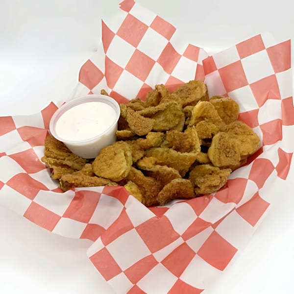 Fried pickles in a red and white checkered paper basket with a side of ranch dressing.