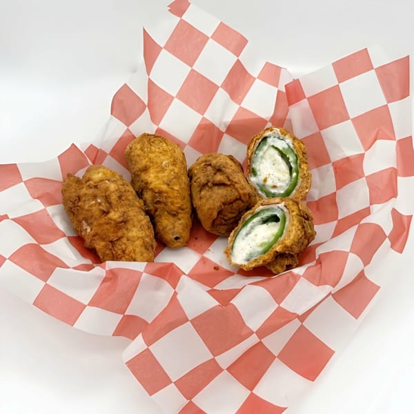 Four fried jalapeño poppers in a red and white checkered paper basket, two cut open.